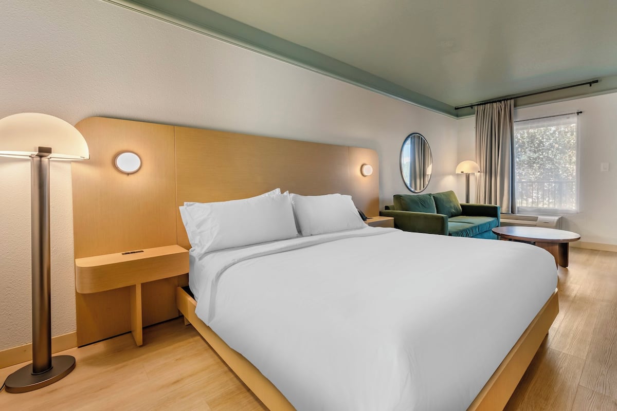 Habitació d'hotel moderna amb un llit gran, tauletes de nit, un mirall rodó, una taula petita rodona i un sofà.