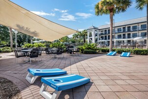 Zona de piscina con sillones, mesas y sombrillas.