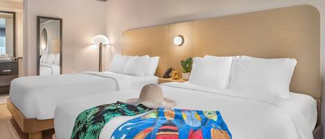 A hotel room with two beds, a large mirror, a bedside lamp, and a colorful blanket.