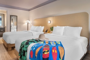 Ein Hotelzimmer mit zwei Betten, einem großen Spiegel, einer Nachttischlampe und einer farbenfrohen Decke.