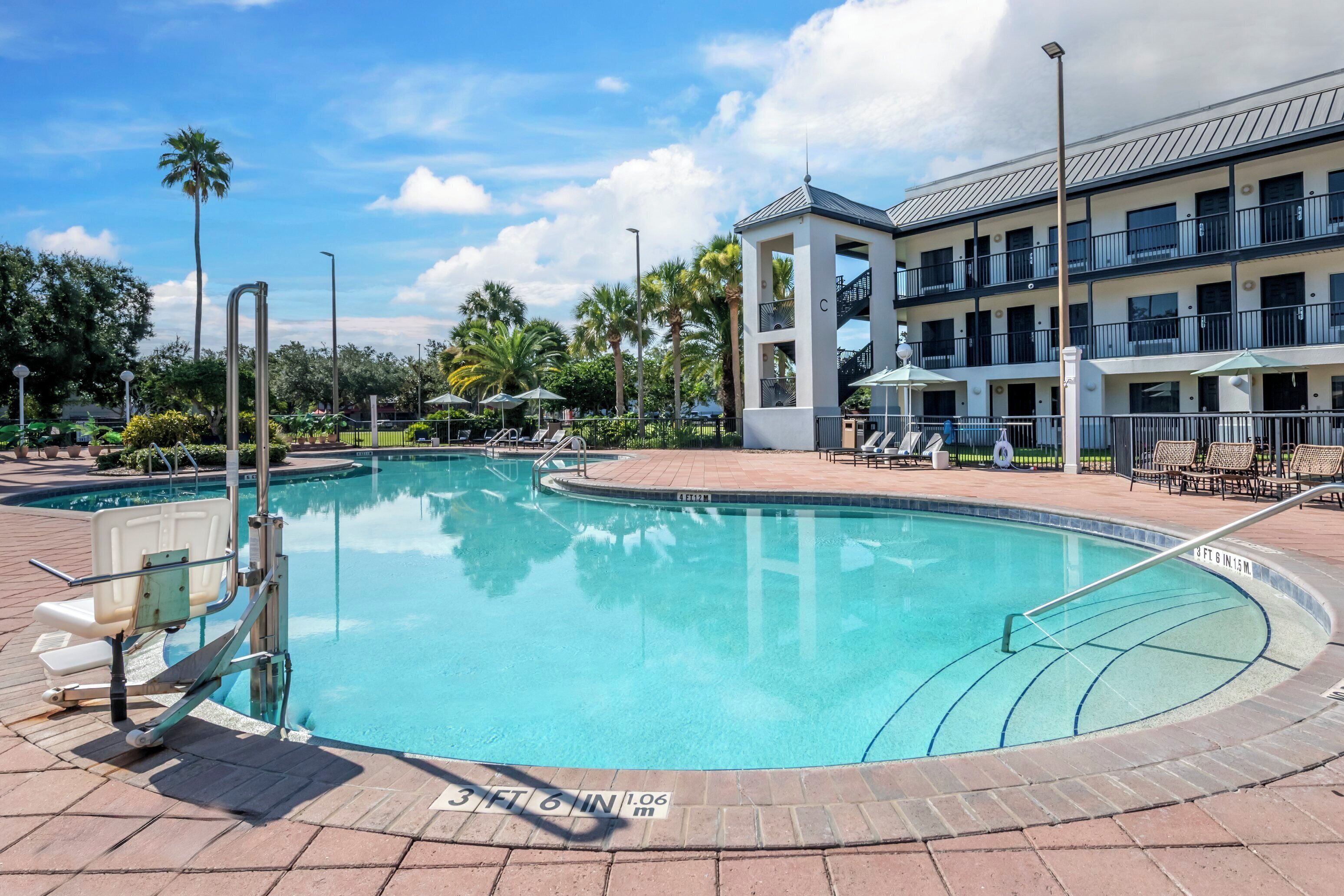 A swimming pool with a clear blue water, surrounded by lounge chairs and umbrellas, with a building in the background.