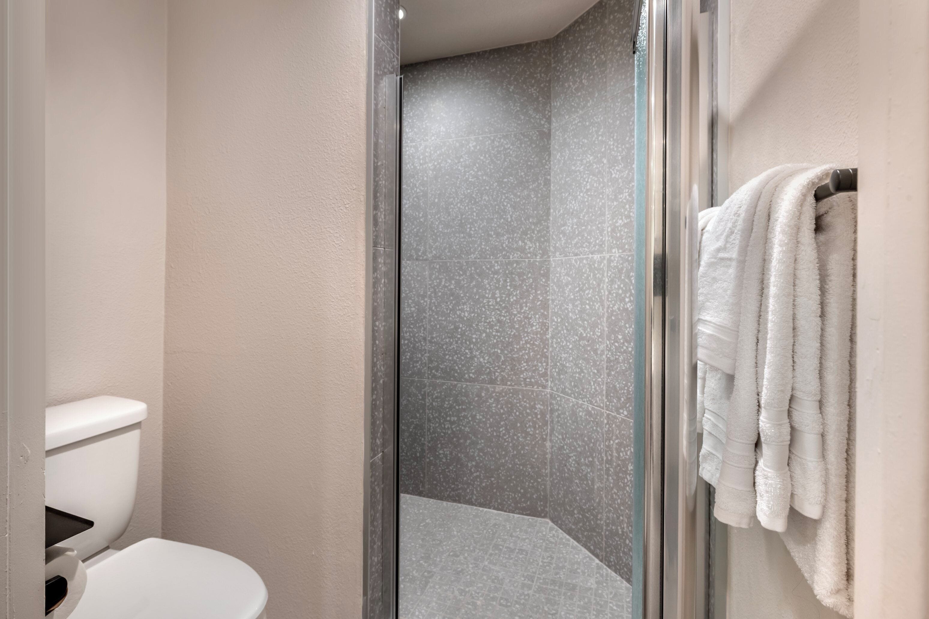 A bathroom with a glass shower enclosure, a toilet, and a towel rack with towels.