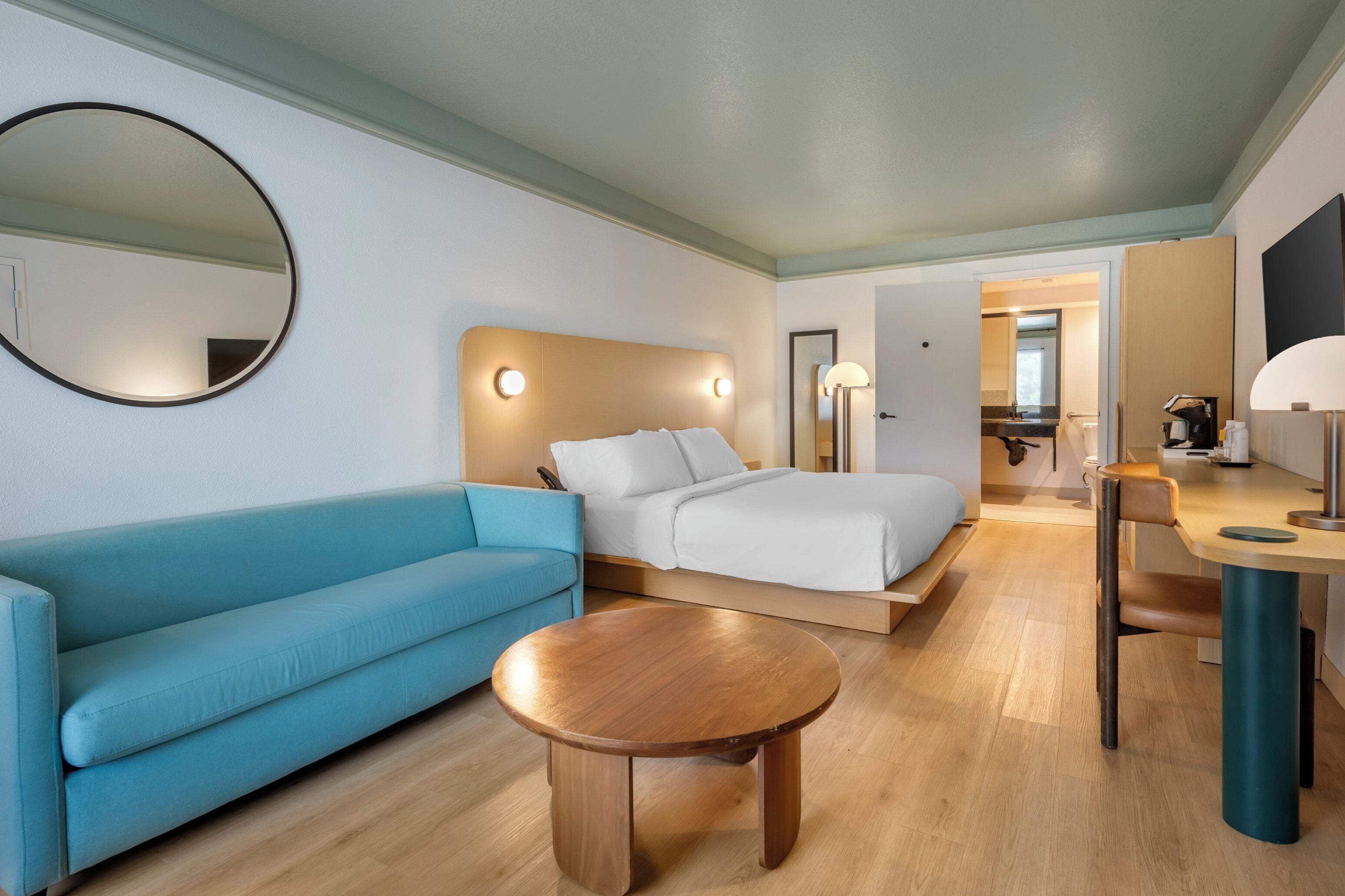 Ein Hotelzimmer mit einem Bett, einem blauen Sofa, einem Holztisch und einem Schreibtisch mit Lampe.