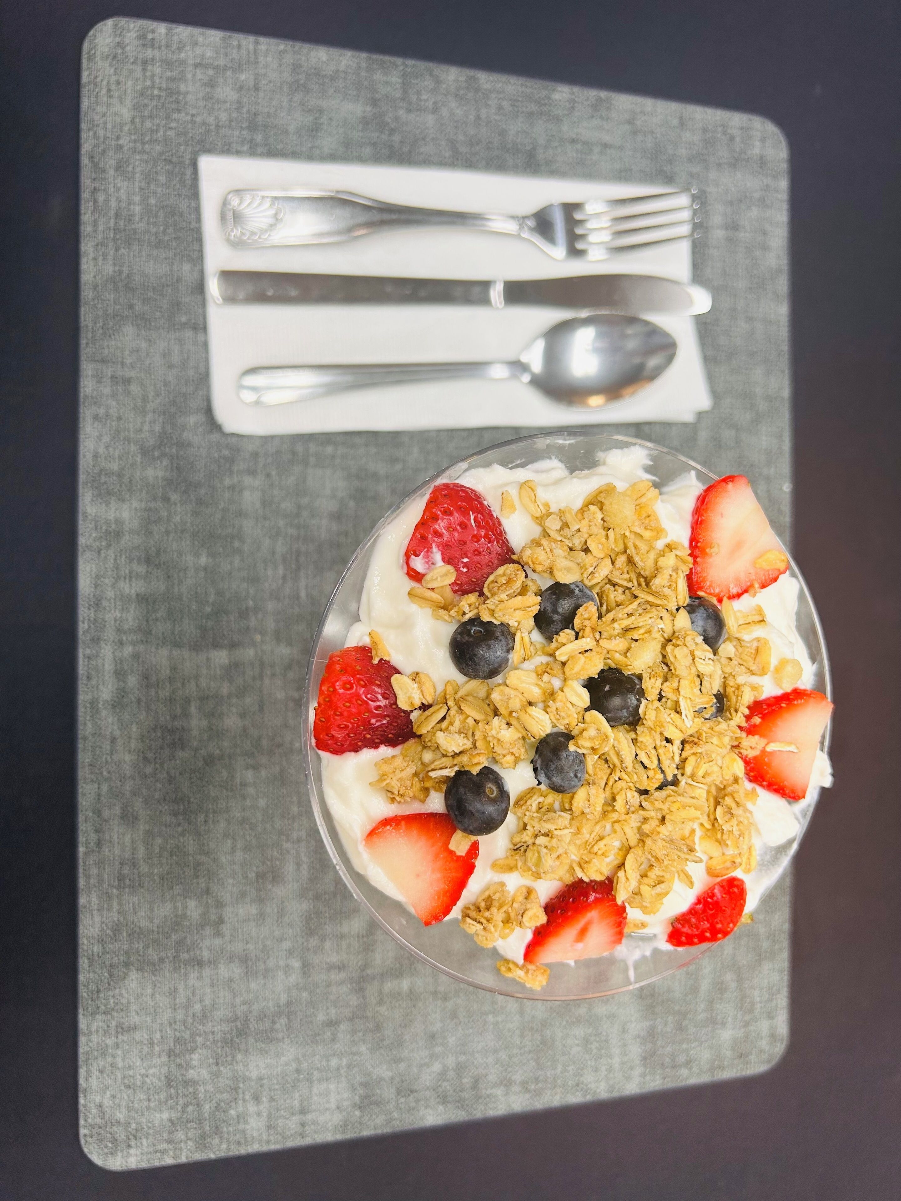 A dessert bowl on a gray placemat with a spoon and fork beside it.