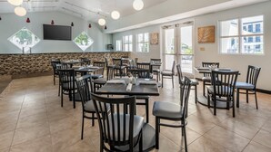 Un ristorante spazioso con numerosi tavoli e sedie, ampie finestre e una televisione a schermo piatto montata sulla parete.