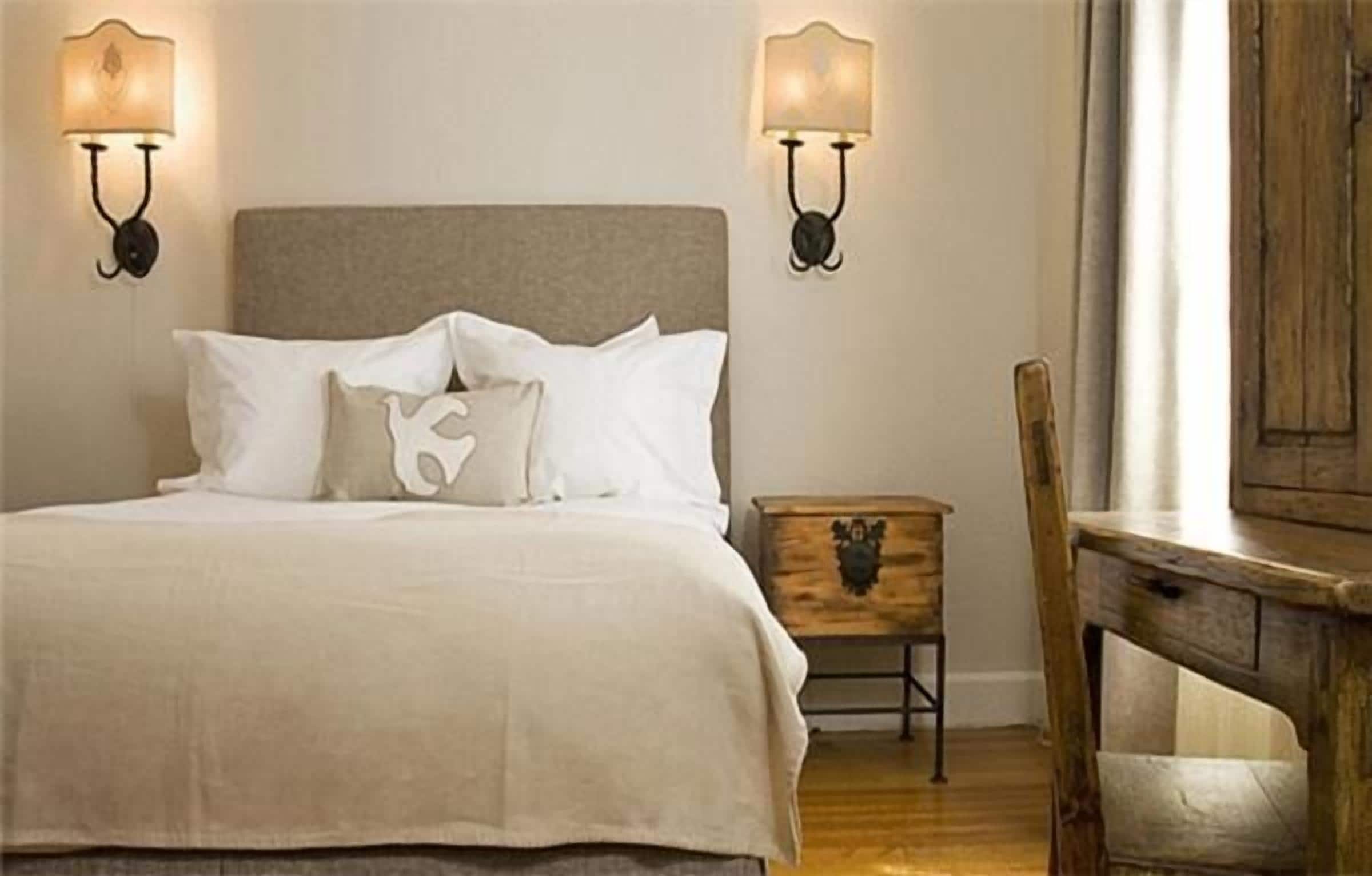 A neatly made bed with white linens and a wooden nightstand beside it.