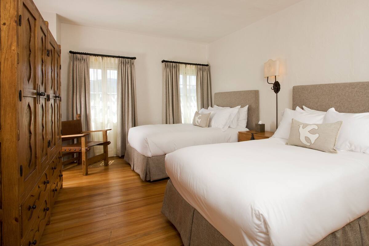 Habitación de hotel con dos camas, armario de madera y mesita de noche con lámpara.