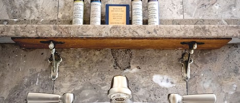 A bathroom with a marble shelf holding various toiletries, a wooden shelf above the sink, and a mirror.