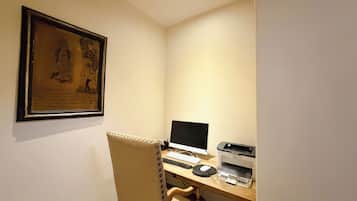 Um pequeno escritório com uma mesa, computador, impressora e um quadro na parede.