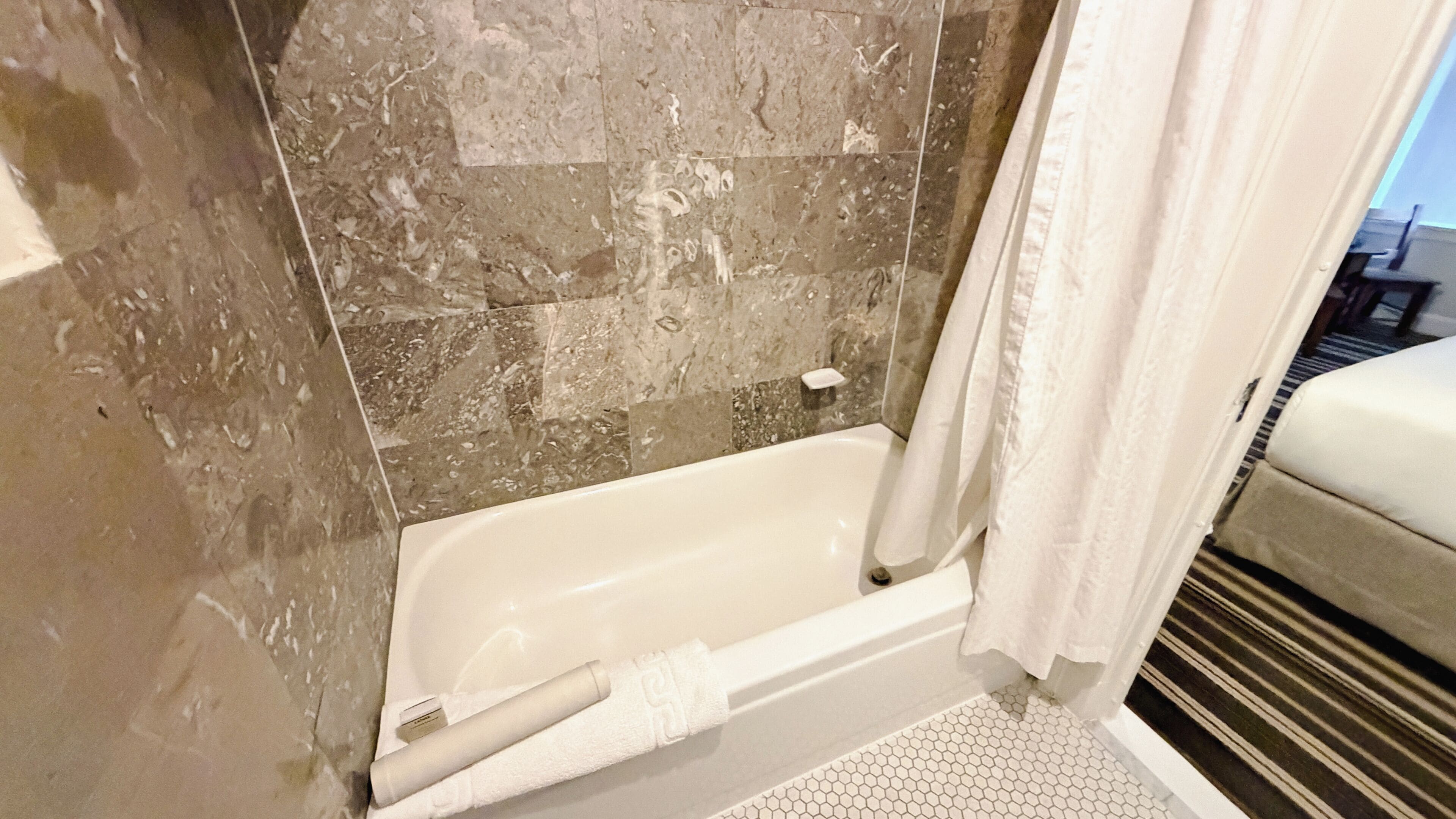 A bathroom with a bathtub, a shower curtain, and a tiled floor.