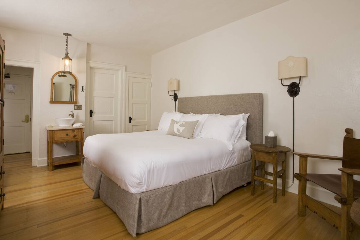 Un dormitorio con una cama grande, una mesita de noche, un espejo, una lámpara y una silla de madera.