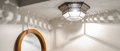 A bathroom with a wooden-framed mirror, a sink with a marble countertop, and a wall-mounted light fixture.
