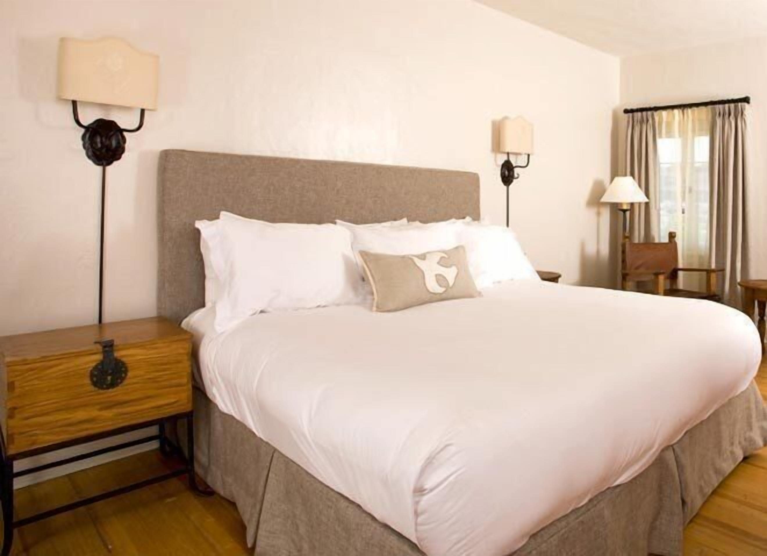 A neatly made bed with white linens and a beige headboard in a hotel room.