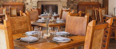 A dining area with wooden tables and chairs, set with plates, glasses, and cutlery.