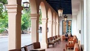Un espace extérieur abrité, doté de colonnes et de tables, donnant sur une rue.