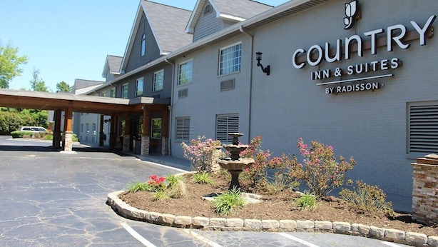 A Country Inn & Suites building with a stone facade, a covered entrance, and a landscaped garden with a fountain.