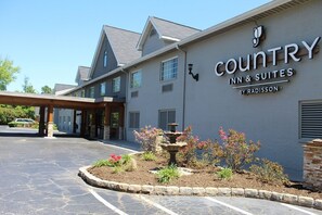 A Country Inn & Suites building with a stone facade, a covered entrance, and a landscaped garden with a fountain. - Country Inn & Suites by Radisson, Charlotte I-85 Airport, NC (Charlotte)