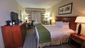 A hotel room with a bed, desk, chair, lamps, and a television.