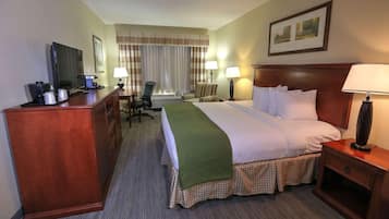 A hotel room with a bed, desk, chair, lamps, and a television.