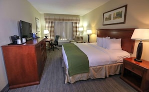 A hotel room with a bed, desk, chair, lamps, and a television.