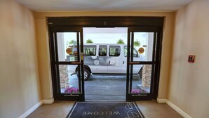 A hotel entrance with a welcome mat, a fire alarm, and a van parked outside.
