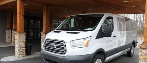 A white Ford van parked under a wooden covered porch with stone pillars.