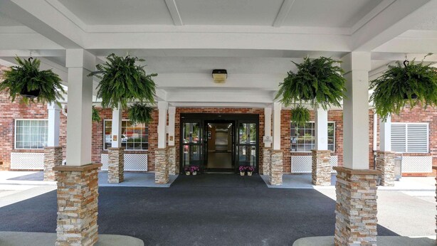 A covered entrance with brick pillars, hanging plants, and a clear pathway leading to the building.