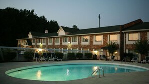 A hotel with a swimming pool, lounge chairs, and a brick facade.
