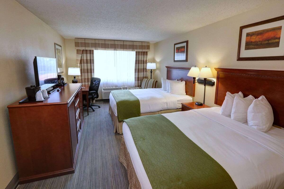 Une chambre d’hôtel avec deux lits, un bureau avec un ordinateur, une chaise et une fenêtre avec des rideaux.