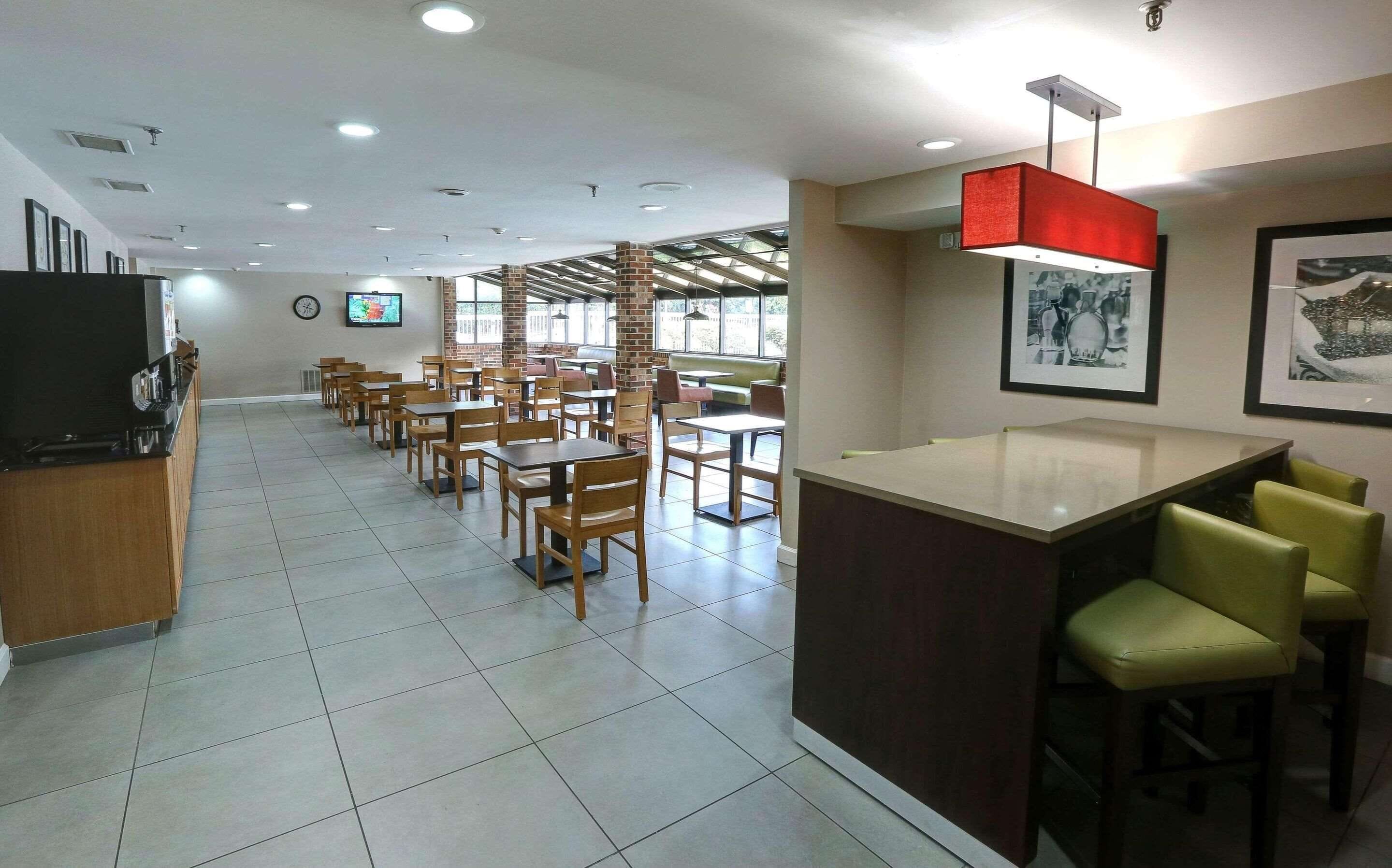 A spacious restaurant with multiple dining tables and chairs, a counter with stools, and a television on the wall.