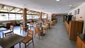 A spacious indoor dining area with multiple tables and chairs, large windows, and a brick column.