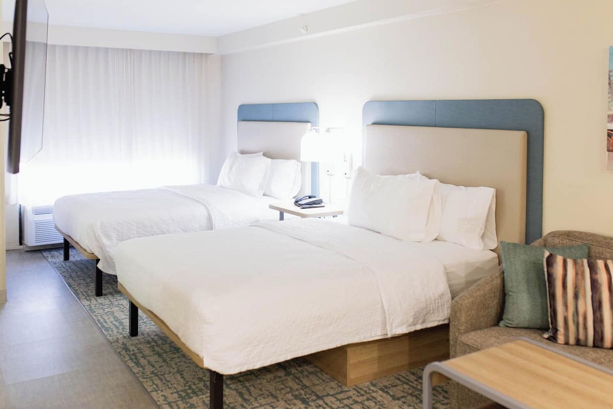A hotel room with two beds, a desk, and a chair.