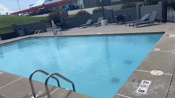 Una piscina con una escalera metálica, sillas de descanso y un solárium empedrado.