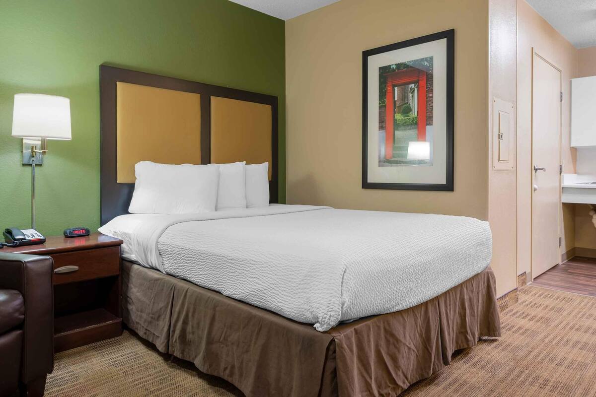 A hotel room with a bed, a nightstand with a lamp, a telephone, and a framed picture on the wall.