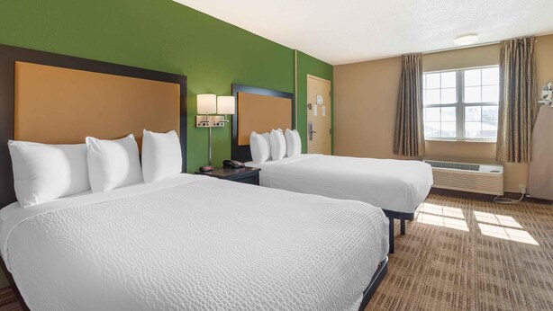 A hotel room with two beds, a large window with curtains, an air conditioning unit, and a lamp on the nightstand. - Extended Stay America Suites Cincinnati Springdale I275 (Cincinnati)