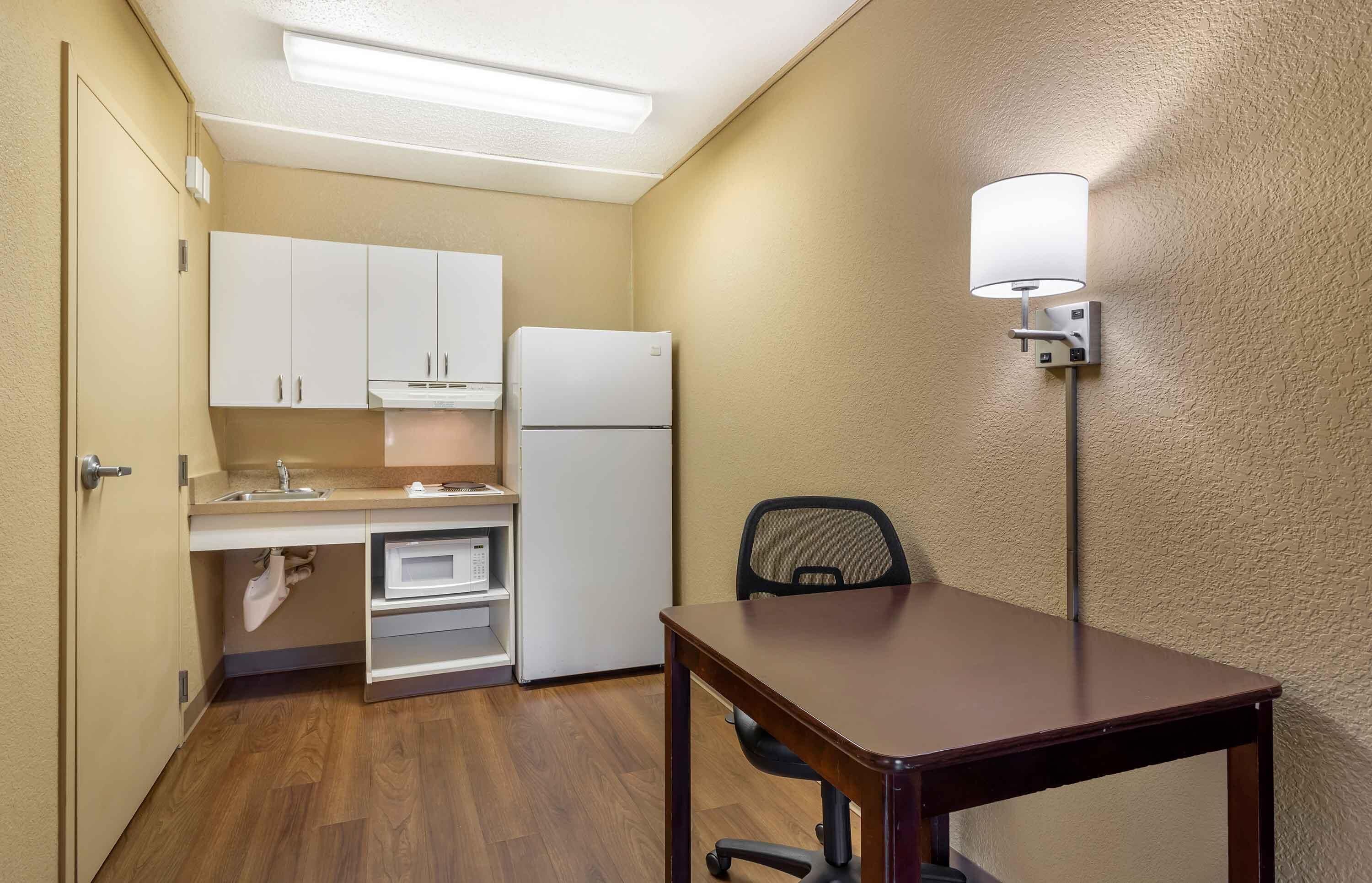 Cocina compacta con armarios blancos, refrigerador, microondas y una mesa con una silla.