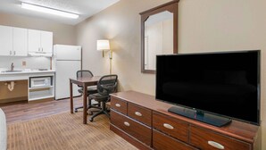 A hotel room with a kitchenette, a flat-screen TV, a wooden dresser, a desk with a chair, and a lamp. - Extended Stay America Suites Cincinnati Springdale I275 (Cincinnati)