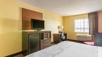 Habitación de hotel con cama, escritorio con silla, televisión, lámpara y ventana con cortinas.