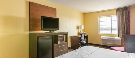 A hotel room with a bed, a desk with a chair, a television, a lamp, and a window with curtains.