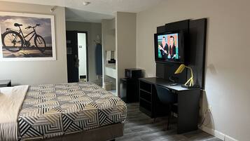 A bedroom with a bed, a desk, a television, and a bicycle painting on the wall.