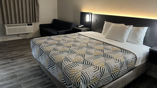 Une chambre d’hôtel comprenant un lit, une table de chevet, une chaise, un radiateur fixé au mur et une fenêtre avec des rideaux.