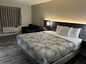 Une chambre d’hôtel comprenant un lit, une table de chevet, une chaise, un radiateur fixé au mur et une fenêtre avec des rideaux.