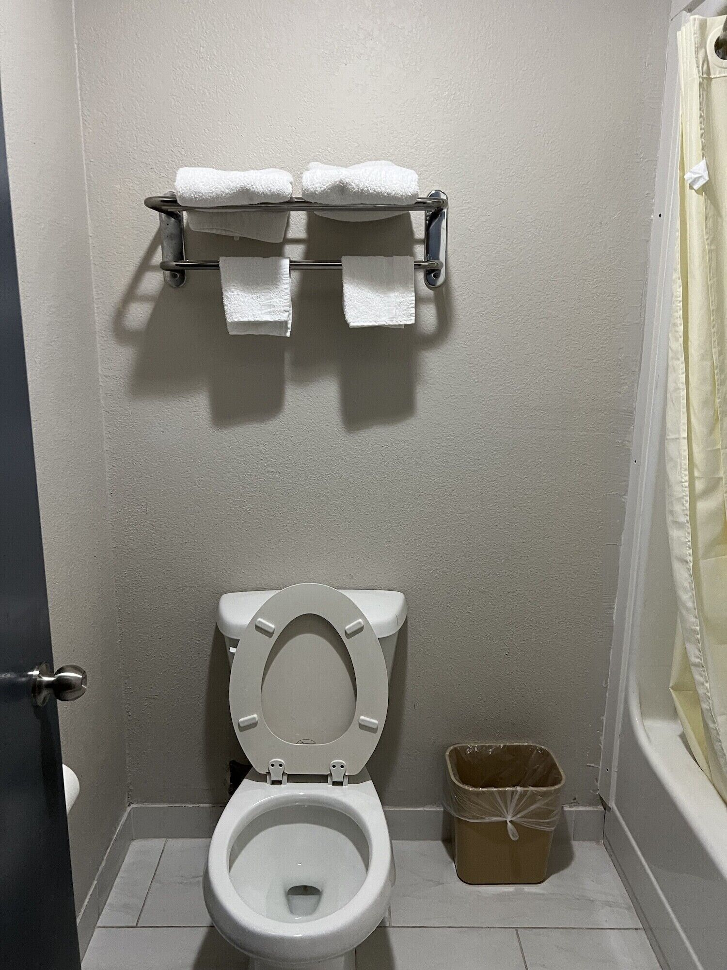 A bathroom with a toilet, a towel rack with towels, and a trash bin.