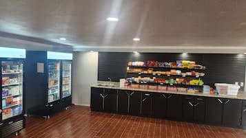 A clean, modern kitchenette with a brick floor, a refrigerator, and a counter stocked with snacks and condiments.