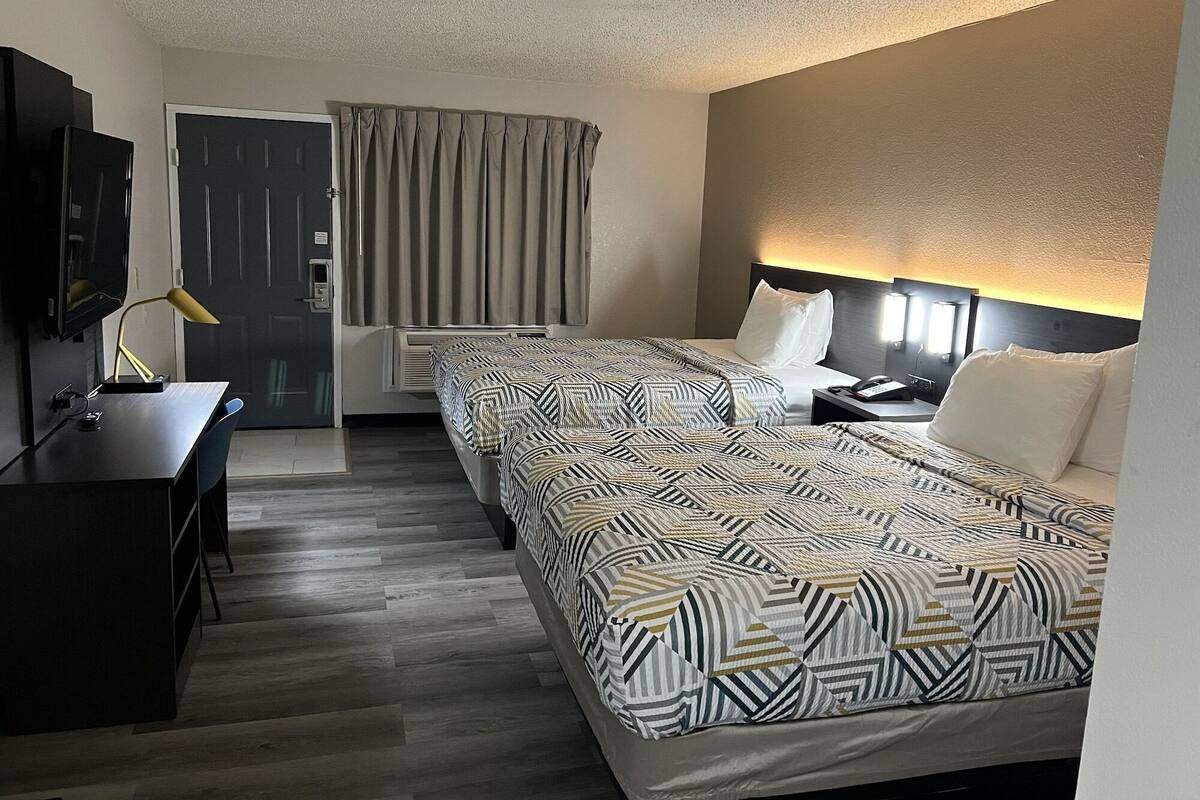 Habitación de hotel con cama, mesita de noche, lámpara, escritorio, televisor y cortinas.