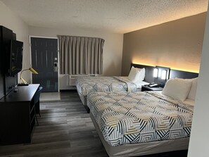 Ein Hotelzimmer mit Bett, Nachttisch, Lampe, Schreibtisch, Fernseher und Vorhängen.