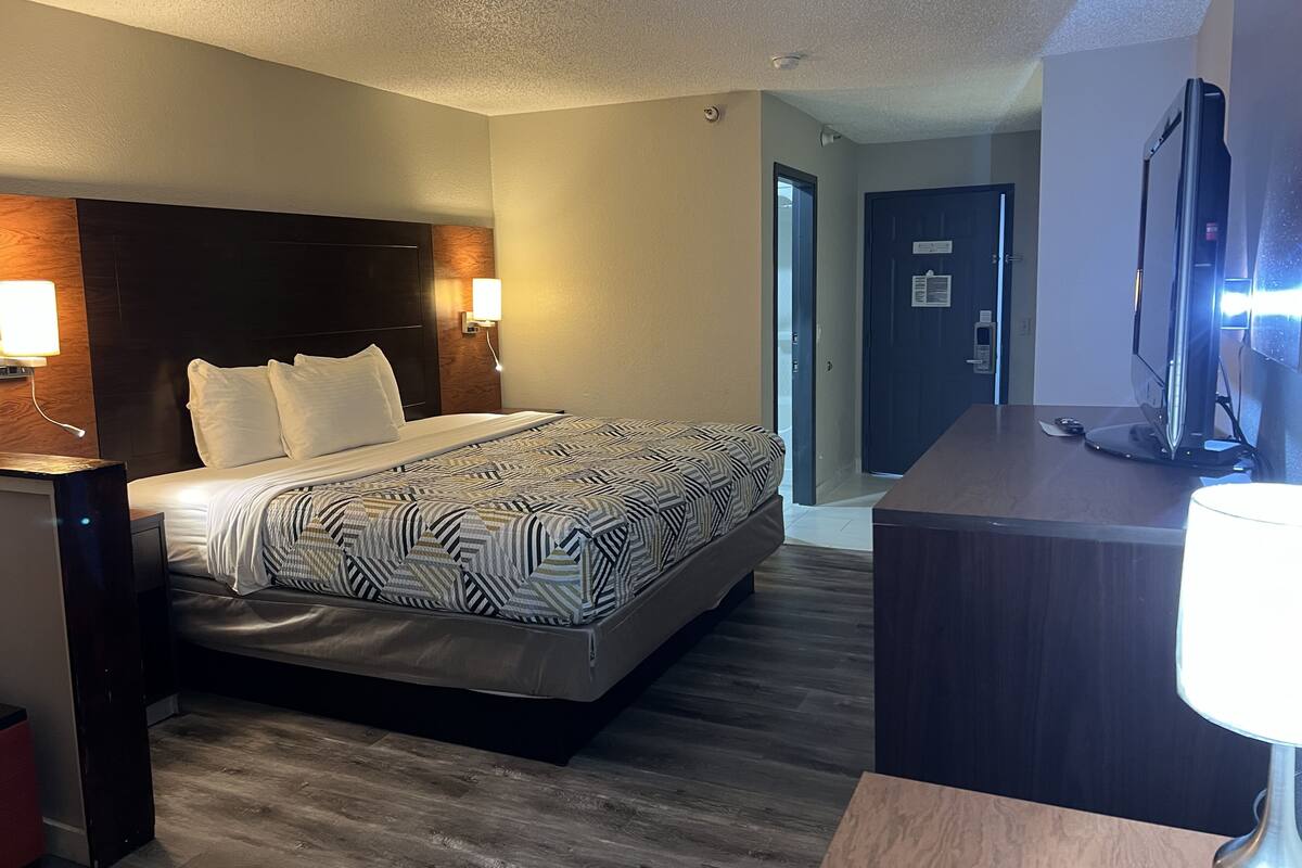 Habitación de hotel con cama, lámparas de noche, escritorio con ordenador y puerta que da a otra habitación.
