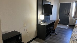 Une chambre d’hôtel équipée d’un téléviseur à écran plat fixé au mur, d’un bureau avec une lampe, d’un four à micro-ondes, d’une chaise et d’un lit à motifs.