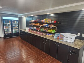 Un área de cocina con despensa integrada llena de refrigerios, un refrigerador y una cesta de productos de lavandería.