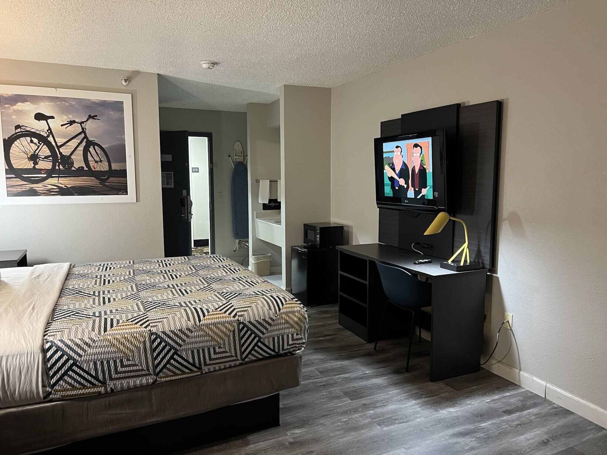 Un dormitorio con una cama, un escritorio, un televisor y un cuadro de bicicleta en la pared.